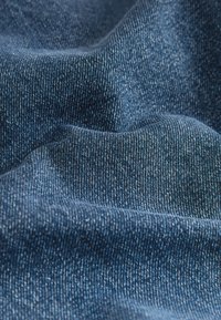 Gros plan d'un tissu en denim bleu plié montrant un tissage texturé et de subtiles variations de couleur.