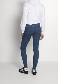 Jeans ajustados de color azul oscuro, fabricados en denim, con una textura suave, costuras sutiles y dos bolsillos traseros con una etiqueta de logo.