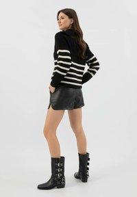 Czarny i biały sweter w pasiaki z długimi rękawami, zestawiony z czarnymi skórzanymi szortami i wysokimi na kolana czarnymi botkami z klamrami.