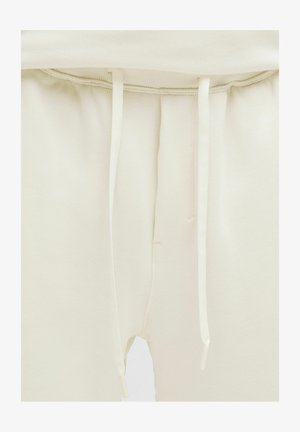 Svetlé krémové teplákové nohavice z jemnej látky. Majú elastický pás s nastaviteľnými šnúrkami a bočné švy pre pohodlné nosenie.