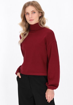 Bordeauxfarbene Rollkragensweater mit lockerer Passform, abgesenkten Schultern und elastischen Bündchen, kombiniert mit lockeren schwarzen Hosen.