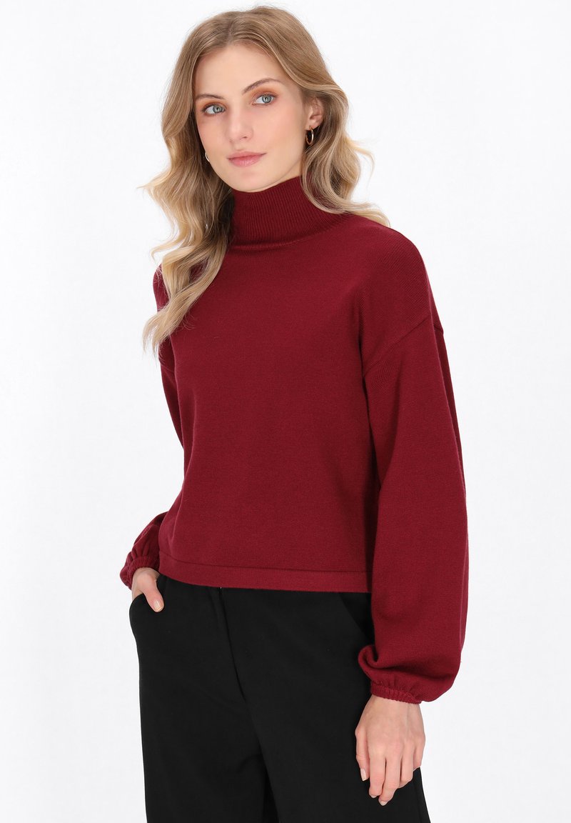 Bordeauxfarbene Rollkragensweater mit lockerer Passform, abgesenkten Schultern und elastischen Bündchen, kombiniert mit lockeren schwarzen Hosen.