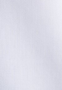 Zbliżenie na białą tkaninę o delikatnej, siateczkowej strukturze splotu i subtelnych cieniach podkreślających wzór tkaniny.