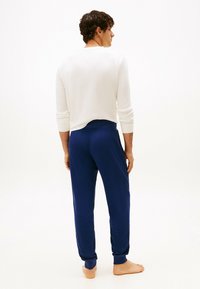 Top bianco a maniche lunghe abbinato a pantaloni della tuta blu navy. Il top ha una texture a costine, mentre i pantaloni hanno una finitura liscia con polsini aderenti.