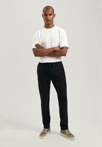 Weißes T-Shirt mit kurzen Ärmeln, kombiniert mit schwarzen Jogginghosen mit Kordelzug und grauen Sneakers. Einfaches Design und einfarbige Farben in lässiger Passform.