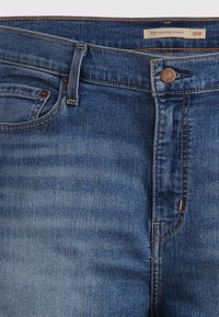 Jeans skinny de cintura alta em denim azul escuro. Apresenta um design clássico de cinco bolsos, botão cobre e costura amarela contrastante.