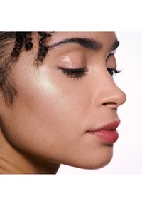 Profielweergave van een gezicht met een gemiddelde huidtint, een zachte textuur, een subtiele highlighter op de wang, donkere wimpers en een zachte roze lipkleur.