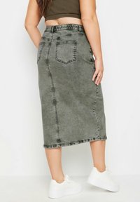 Harmaa farkku midi-hame joustavalla vyötäröllä, jossa on kaksi takataskua ja raaka helma. Yhdistetty valkoisiin lenkkareihin, mikä korostaa rentoa tyyliä.