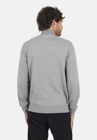 Szary sweter z dzianiny z długimi rękawami i wysokim kołnierzem, z prążkowanym dołem. Tkanina ma gładką, miękką teksturę.