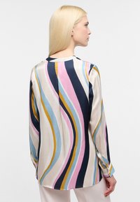 Langærmet bluse med et multifarvet bølgemønster i creme, marineblå, pink og gul. Fremstillet af glat, let stof med en rund krave.