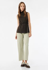 Mustaton tummanruskea toppi korkean kaula-aukon ja vyötärönauhan kanssa, yhdistettynä vaaleanvihreisiin leveälahkeisiin farkkuihin ja tummanruskeisiin lenkkarit.