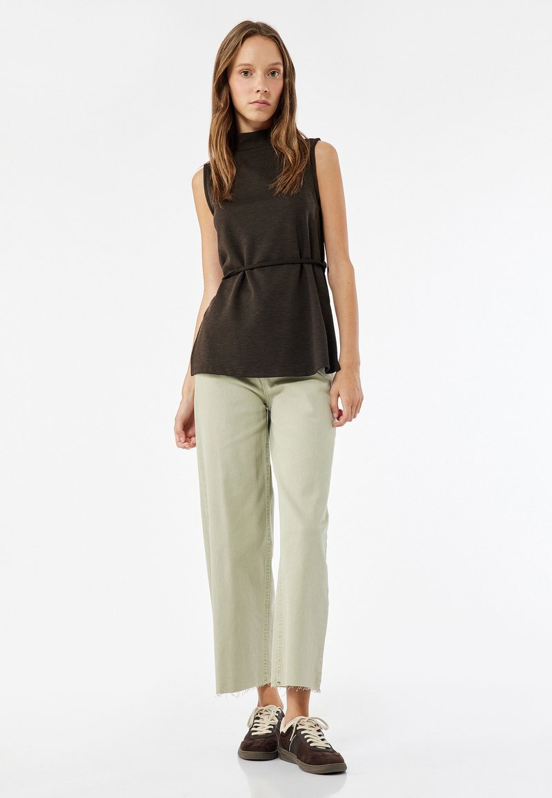 Mustaton tummanruskea toppi korkean kaula-aukon ja vyötärönauhan kanssa, yhdistettynä vaaleanvihreisiin leveälahkeisiin farkkuihin ja tummanruskeisiin lenkkarit.