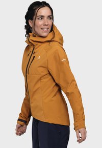 Wasserdichte orangefarbene Jacke mit Kapuze, tailliertem Design, schwarzen Reißverschlussdetails und verstellbaren Bündchen. Der Stoff hat eine glatte Textur und matte Oberfläche.