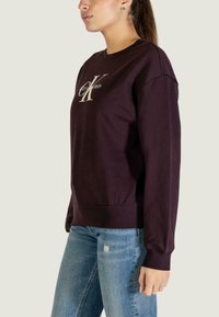 Bluza Calvin Klein w ciemnym fioletowym kolorze, z okrągłym dekoltem i haftowanym logo w kremowym odcieniu. Miękki materiał z ściągaczami na mankietach i dole.