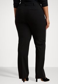 Čierne nohavice s rovnými nohavicami, s dvoma zadnými vreckami a hladkou textúrou. Nosené s čiernymi ihlovými topánkami.