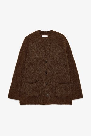 Brūna kardigana, kas izgatavota no pūkainas, teksturētas auduma. Tam ir V veida kakla izgriezums, garas piedurknes, piecas melnas pogas un divas priekšējās kabatas.
