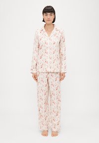 Conjunto de pijama floral com mangas longas e calças, feito de tecido macio. Padrão rosa claro e creme com pequenos motivos florais.