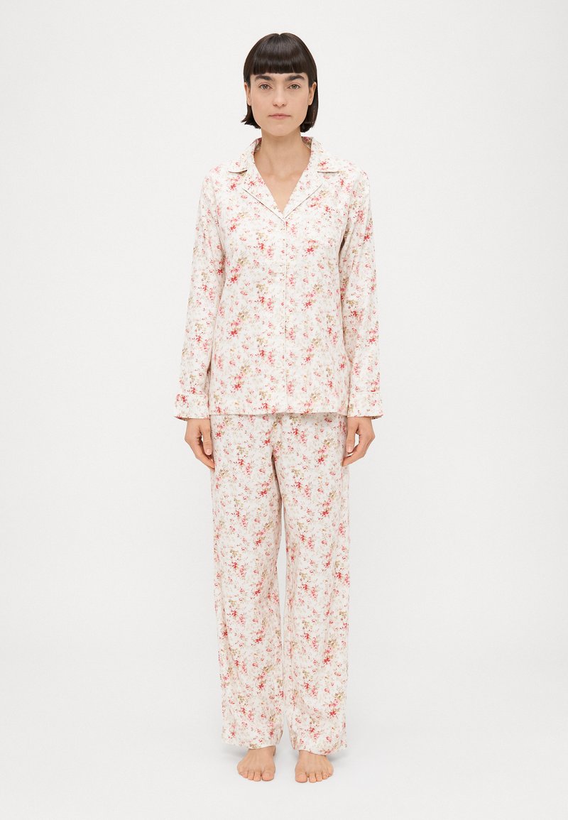 Conjunto de pijama floral com mangas longas e calças, feito de tecido macio. Padrão rosa claro e creme com pequenos motivos florais.