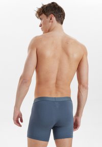 Herrebokserummer i mørkeblå stof med en blød talje. Designet er tætsiddende og fremhæver en glat tekstur og rene linjer.