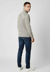 Suéter gris con cuello alto, tejido texturizado, combinado con jeans azul oscuro y zapatillas blancas. Vista desde atrás, mostrando el conjunto.