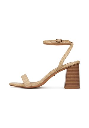 Beige szőtt bőr szandál blokk sarkal, nyitott orral és arany csattal ellátott boka pánttal fehér háttérrel.