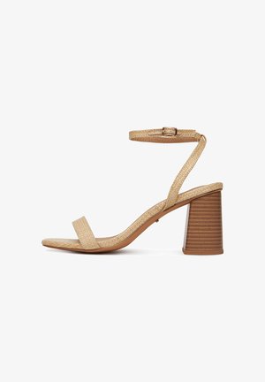 Beżowe plecione skórzane sandały na słupku, z otwartym noskiem i paskiem na kostce z złotą klamrą na białym tle.