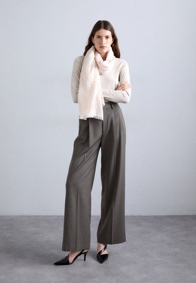 Helles beiges Langarmoberteil, rosa gepunkteter Schal, graue weit geschnittene Hose und schwarze High Heels. Sanfte Texturen und einfache Silhouetten.