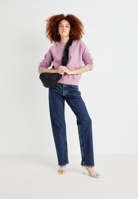 Lys rosa hettegenser med en teksturert svart clutch, mørkeblå høy midje jeans og beige stroppesandaler. Krøllete hår stylet løst.