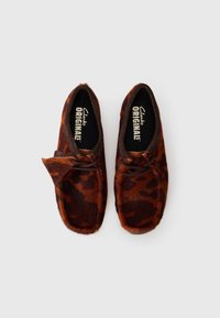 Brown slip-on shoes made of soft fur with a leopard print pattern, featuring a rounded toe and a decorative leather bow on the upper.