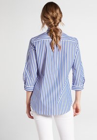 Camicia a maniche lunghe azzurra e bianca a righe con maniche arrotolate a tre quarti, orlo curvo e texture del tessuto liscia.