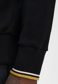 Manica di felpa blu navy con texture a coste e polsino a strisce con accenti gialli, bianchi e blu navy.