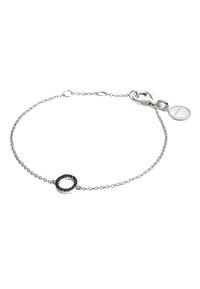 Pulsera de cadena de plata con un acento de piedra negra circular, con un cierre tipo langosta y una pequeña etiqueta redonda adherida.