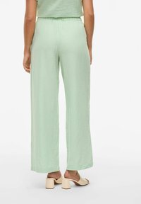 Lichtgroene, comfortabele broek van textuurstof. Heeft een elastische tailleband en wijde pijpen, gecombineerd met beige block-heeled muiltjes.