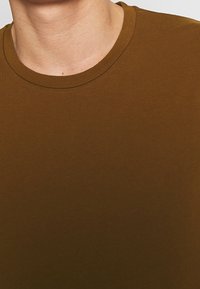Camiseta de algodón marrón con cuello redondo, textura suave y un diseño simple. El primer plano se centra en el cuello y los detalles de la tela.