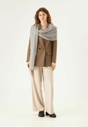 Blazer marron, écharpe gris clair à texture subtile, pantalon large beige et chaussures noires. La tenue combine des couleurs neutres et des tissus doux.
