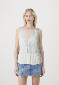 Lys grå, plissert tanktop med dyp V-hals og justerbar knytning i midjen, sammen med et denim-miniskjørt med frynsete kant.