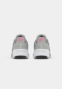 Aizmugures skats uz pelēkām un rozā Reebok sporta apaviem ar baltām zālēm un melnu profilu uz baltas fona.