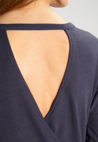 Baksidan av en person som bär en mörkblå topp med en triangulär öppning på ryggen som visar övre delen av ryggen och axeln.