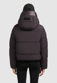 Mørk lilla pufferjakke med høj krave, der har et mærket label på hætten og en quiltet tekstur. Minimalistisk design, cropped pasform.