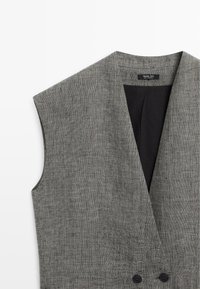 Šedá texturovaná vesta bez rukávů s hlubokým výstřihem do V, dvouřadým zapínáním a černou podšívkou od Massimo Dutti.