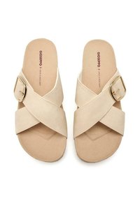 Sandalias de tira cruzada beige hechas de ante suave con un acento de hebilla dorada. Plantillas texturizadas para mayor comodidad y un diseño de suela plana.