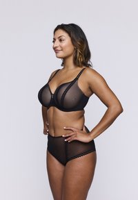 Sostén negro y bragas de talle alto hechas de malla transparente con borde de encaje con forma de ondas, que ofrecen una silueta suave y contorneada. Tirantes ajustables.