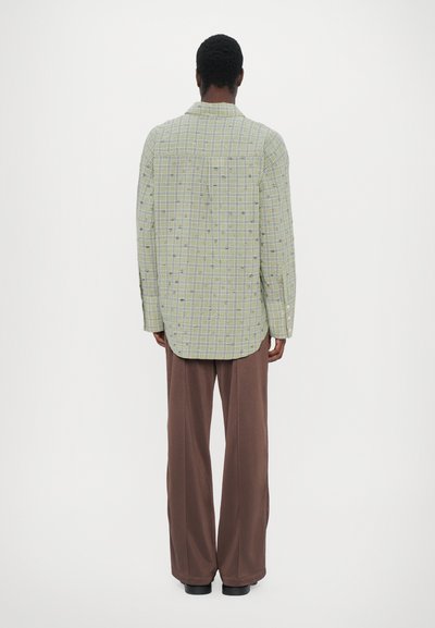 Green checkered shirt with long sleeves, button-down collar, and boxy fit, paired with brown wide-leg trousers. Simple design with no embellishments.