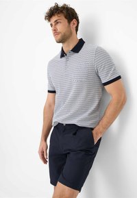 Polo shirt con colletto caratterizzato da un motivo geometrico blu e bianco, abbinato a pantaloni corti blu scuro. Vestibilità slim con maniche corte e dettagli a coste.