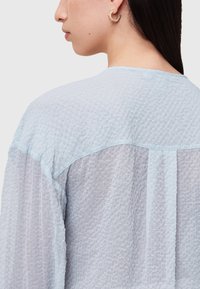 Helles blaues, texturiertes Blusenshirt mit einer glatten Passe und transparenter Stoff; sie zeichnet sich durch eine lockere Passform und ein dezentes kariertes Muster aus, das elegante Einfachheit zeigt.