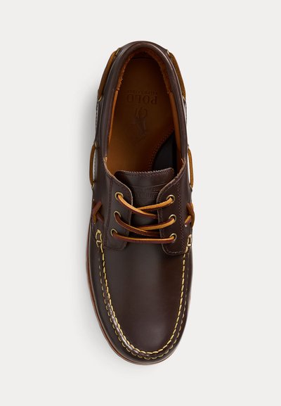 Brun båtsko i skinn med beige lisser, kontrasterende gule sømmer og Polo Ralph Lauren-logo på innersålen, sett ovenfra.