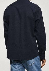 Chemise bleu marine à manches longues avec col boutonné, tissu texturé et ourlet arrondi. Comprend des poignets boutonnés et un design uni.