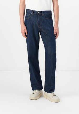 Dark blue denim jeans with straight legs, five-pocket design, and visible stitching. Worn with off-white sneakers.