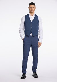 Blaues maßgeschneidertes Weste mit fünf Knöpfen, kombiniert mit passenden Hosen. Darunter ein weißes Hemd. Schwarze elegante Schuhe runden das Outfit ab.