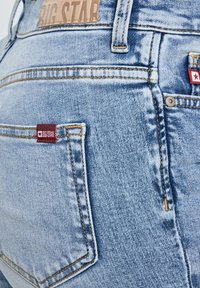 Hele sinised teksapüksid, millel on Big Star brändi nahast silt ja tagataskutel punased kangast sildid, näidates õmblusi ja metallist ninnikuid.